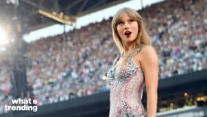 Taylor Swift performing on stage in a sparkling dress with a large crowd in the background
