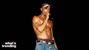 Tupac Shakur shirtless performing with a microphone, wearing a blue bandana and jeans with a studded belt.