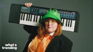 Person wearing a green frog hat and glasses holding a Casio CA-110 keyboard over their shoulder