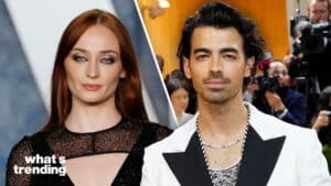 Sophie Turner in a black dress and Joe Jonas in a white suit at a red carpet event with photographers behind.