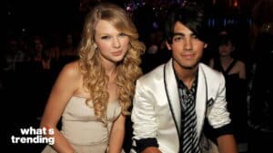 Taylor Swift and Joe Jonas sitting together at an event, Taylor in a strapless dress and Joe in a white blazer with a striped tie