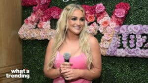 Blonde woman in pink dress holding microphone in front of floral wall with "what's trending" logo