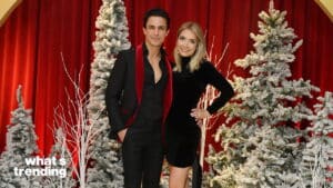 Man and woman posing in front of snowy Christmas trees and red curtain backdrop at a holiday event