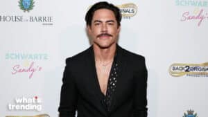 Man with mustache wearing black suit and patterned shirt at event with House of Barrie backdrop