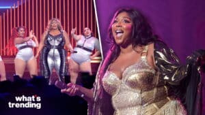 Lizzo performing on stage with backup dancers in silver outfits and a sparkling gold costume under purple lighting