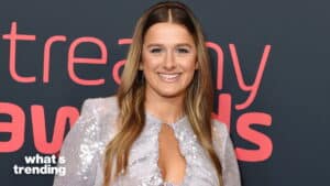 Young woman with long hair wearing a silver sequin dress smiling at a What's Trending event backdrop