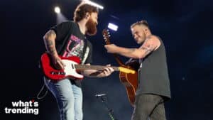 Two tattooed male musicians playing guitars on stage under bright lights