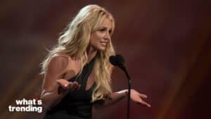 Britney Spears speaking at a microphone with a questioning gesture on stage