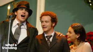 Ashton Kutcher, Danny Masterson, and Mila Kunis smiling together on stage at a formal event