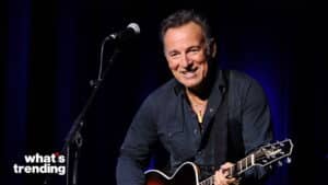 Bruce Springsteen smiling while playing a Takamine guitar on stage with a microphone nearby