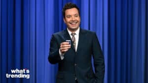 Jimmy Fallon smiling and holding a remote control on a blue curtain stage with "what's trending" text.