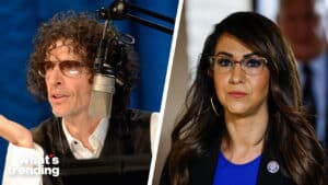 Howard Stern speaking into a microphone and Congresswoman Lauren Boebert wearing glasses and a blue top.