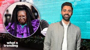 Hasan Minhaj smiling in front of a digital screen with an inset photo of Whoopi Goldberg in a purple outfit.