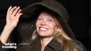 Smiling woman with long blonde hair wearing a large green plaid hat and matching coat against a black background