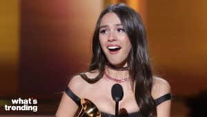 Olivia Rodrigo holding a Grammy award and speaking at a microphone during an awards ceremony