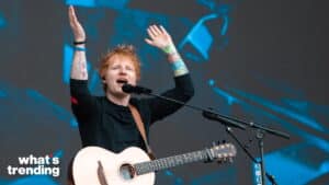 Ed Sheeran singing and playing guitar on stage with hands raised during a live performance
