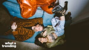 Two people lying on a blue couch, one wearing a tiger-striped jacket and the other in a fur coat and patterned pants with black boots.