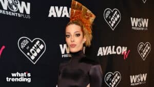 Person with styled orange hair wearing a black turtleneck dress at a House of Love and Avalon TV event backdrop