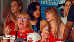 Taylor Swift clapping next to a woman in a Kansas City Chiefs jersey at a sports event.