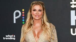Blonde woman in a sparkly gold dress posing at a What's Trending event with a black background and colorful logo.