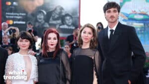 Four people dressed formally posing on a red carpet with photographers in the background