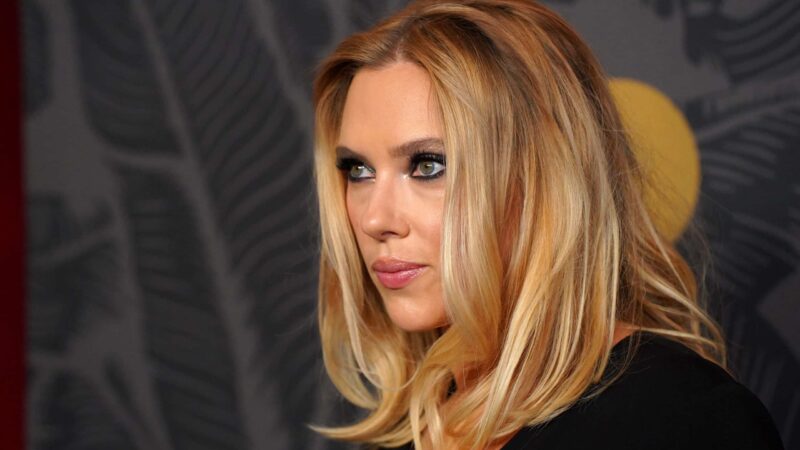Scarlett Johansson with blonde hair and smoky eye makeup looking to the side against a patterned background