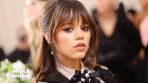 Close-up of a young woman with brown hair and bangs wearing a black outfit with a bow detail.