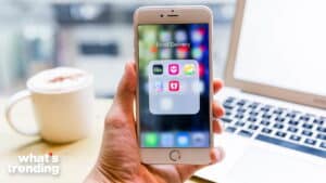 Hand holding iPhone displaying a folder named Food Delivery with Uber Eats, foodpanda, and other app icons, laptop and coffee cup in background.