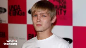 Young man with blonde hair and blue eyes wearing a white shirt at a red and white checkered event backdrop
