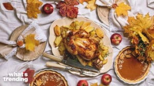 Roasted whole chicken with potatoes, pumpkin pies, apples, and autumn leaves on a white tablecloth.