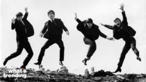 The Beatles jumping in the air on a rooftop in black suits in a black and white photo