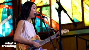 Woman singing and playing an electric guitar with flame designs in front of colorful stained glass windows