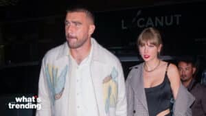 Taylor Swift in a black top and checkered coat walking beside a man in a white patterned jacket at night
