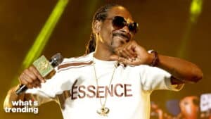 Snoop Dogg wearing an Essence shirt and sunglasses, holding a microphone on stage.