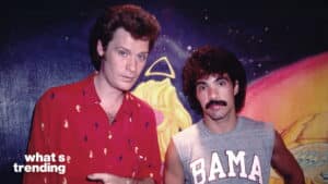 Hall and Oates posing in front of colorful mural, Hall wearing red shirt and Oates in gray sleeveless "BAMA" shirt