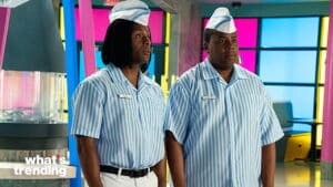 Two men wearing blue and white striped diner uniforms and paper hats standing inside a colorful diner.