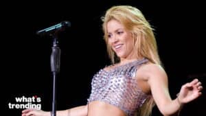 Shakira performing on stage wearing a silver metallic crop top near a microphone stand