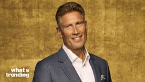 Smiling man in a gray suit and white shirt against a textured gold background with "what's trending" logo