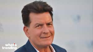 Charlie Sheen smiling in a blue blazer against a blurred background with "what's trending" text.