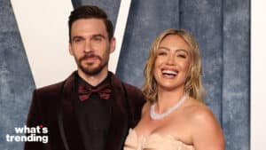 Hilary Duff and Matthew Koma smiling at a formal event with Hilary wearing a pearl necklace and strapless dress.