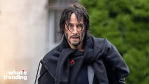 Keanu Reeves with wet hair wearing a black jacket and hoodie outdoors in the rain