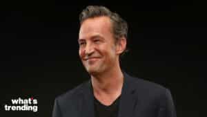Matthew Perry smiling in a black blazer and shirt against a black background with "what's trending" text.