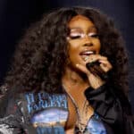 Singer SZA performing on stage with curly hair and star-shaped eye makeup.