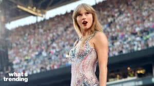 Taylor Swift performing on stage in a sparkling dress with a large crowd in the background