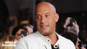Vin Diesel wearing a white jacket at a public event with fans in the background.