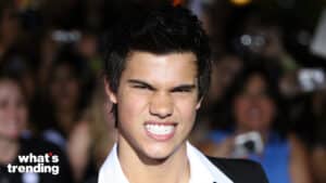 Taylor Lautner grimacing at a public event with blurred crowd and cameras in the background