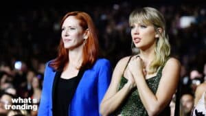 Taylor Swift standing with a woman in a blue blazer at a crowded event, both looking intently forward