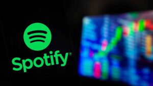In this photo illustration, the Spotify logo is displayed on a smartphone screen, with graphic representation of the stock market in the background.