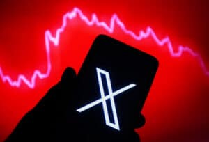 Smartphone displaying the X logo with a red background showing a declining stock market graph
