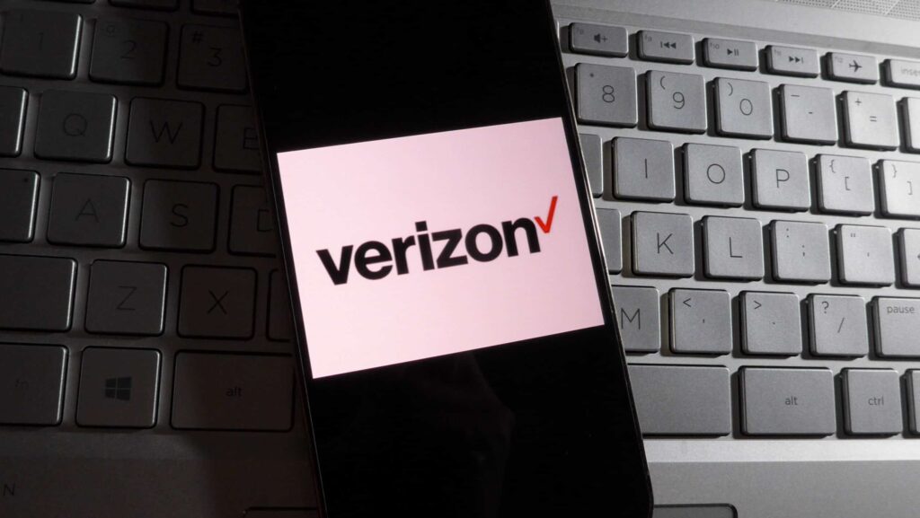 In this photo illustration, Verizon logo is displayed on a smartphone with a workplace background.